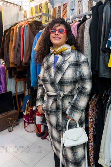 Vertical Portrait of a woman wearing jacket and sunglasses trying on clothes in a second hand store