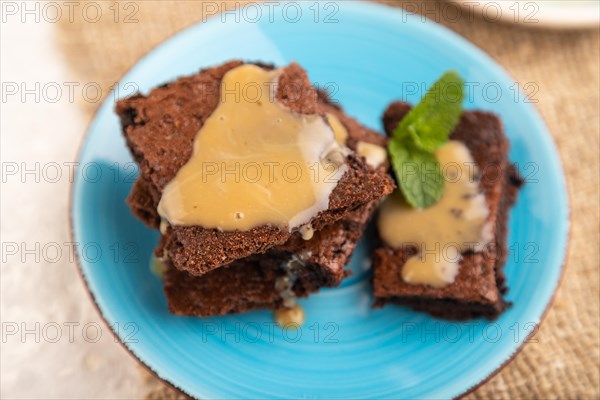 Chocolate brownie with caramel sauce with a cup of coffee on gray concrete background and linen textile. side view, close up, selective focus