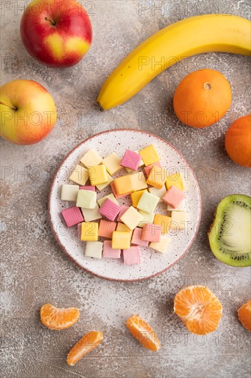 Various fruit jelly chewing candies on plate on brown concrete background. apple, banana, tangerine, top view, flat lay, close up