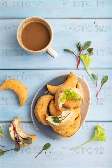 Homemade salted crescent-shaped cheese cookies, cup of coffee on blue wooden background. top view, flat lay, close up