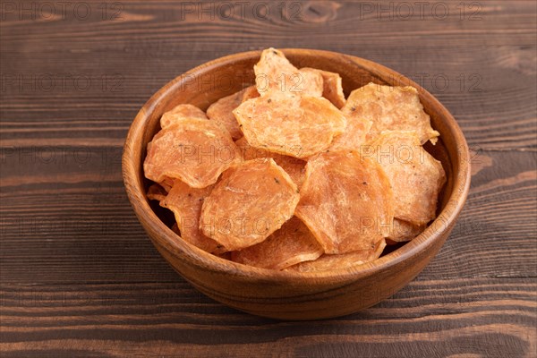 Slices of dehydrated salted meat chips with herbs and spices on brown wooden background. Side view, close up