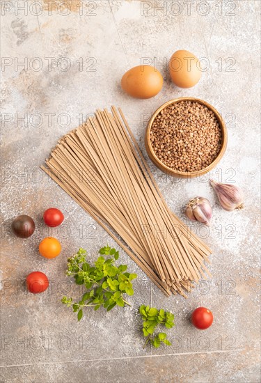 Japanese buckwheat soba noodles with tomato, eggs, spices, herbs on brown concrete background. Top view, flat lay, close up