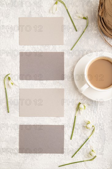 Gray paper business card mockup with spring snowdrop galanthus flowers and cup of coffee on gray concrete background. Blank, business card, top view, flat lay, copy space, still life. spring concept