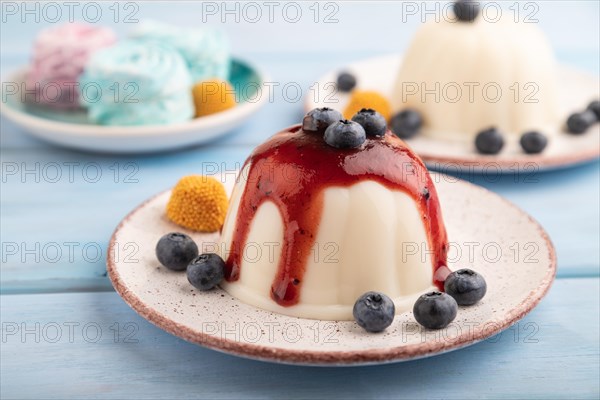 White milk jelly with blueberry jam on blue wooden background and blue linen textile. side view, close up, selective focus