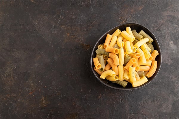 Rigatoni colored raw pasta with tomato, eggs, spices, herbs on black concrete background. Top view, flat lay, copy space