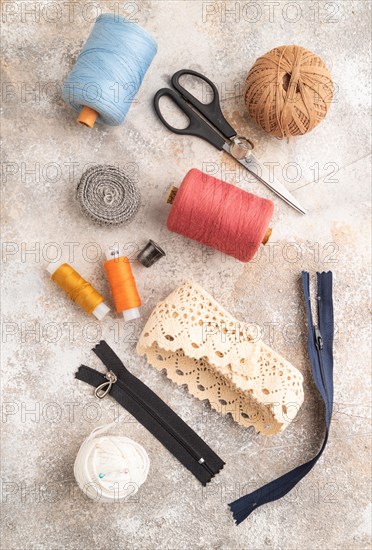 Sewing accessories: scissors, thread, thimbles, braid on brown concrete background. Top view, flat lay