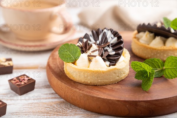 Sweet tartlets with chocolate and cheese cream with cup of coffee on a white wooden background and linen textile. side view, close up, selective focus