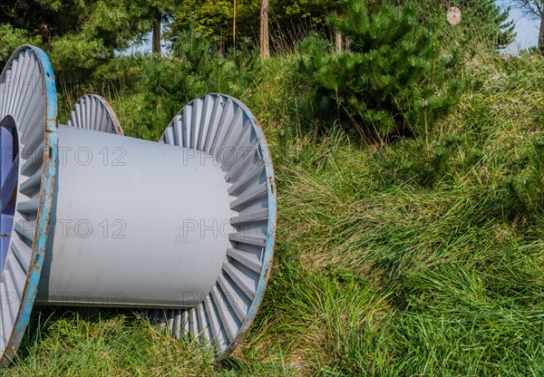 Large metal industrial spools sitting on grassy hillside