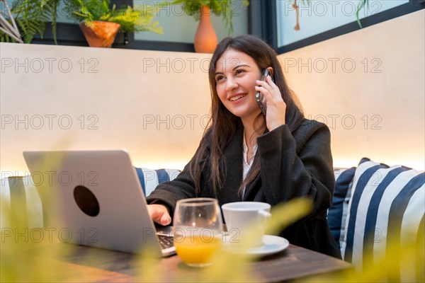 Smiling young businesswoman attending a call while working with laptop in a cafeteria