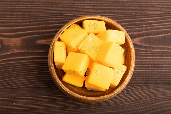 Dried and candied mango cubes in wooden bowls on brown wooden textured background. Top view, flat lay, close up, vegan, vegetarian food concept