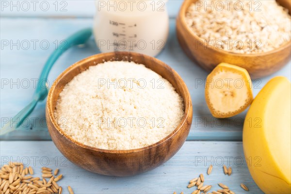 Powdered milk and oatmeal, banana baby food mix, infant formula, pacifier, bottle, spoon on blue wooden background. Side view, selective focus, artificial feeding concept