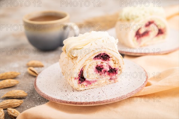 Roll biscuit cake with cream cheese and jam, cup of coffee on brown concrete background and orange linen textile. side view, close up, selective focus