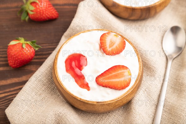 Grained cottage cheese with strawberry jam on brown wooden background and linen textile. side view, close up, selective focus