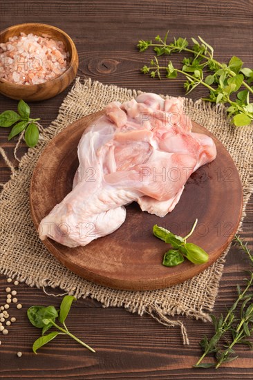Raw turkey wing with herbs and spices on a wooden cutting board on a brown wooden background and linen textile. Side view, close up