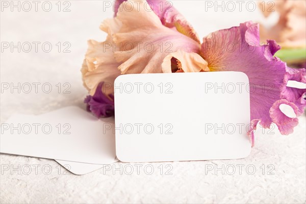 White business card with iris purple flowers on white concrete background. side view, copy space, mockup, template, spring, summer minimalism concept