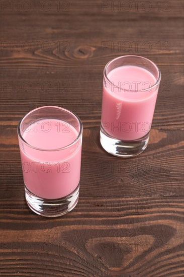 Sweet strawberry liqueur in glass on a brown wooden background. side view, close up