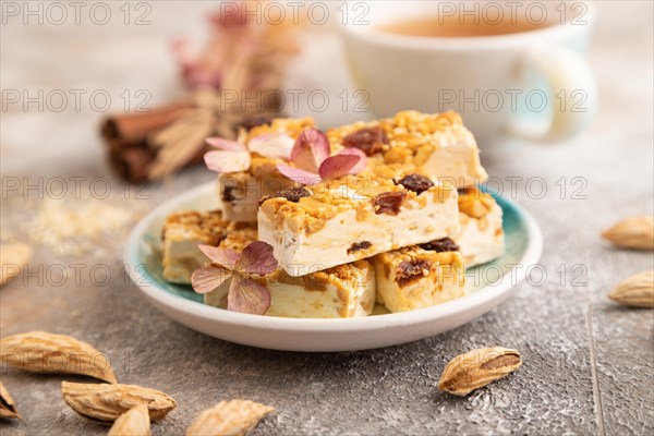 Traditional candy nougat with nuts and sesame with cup of green tea on brown concrete background. side view, close up, selective focus