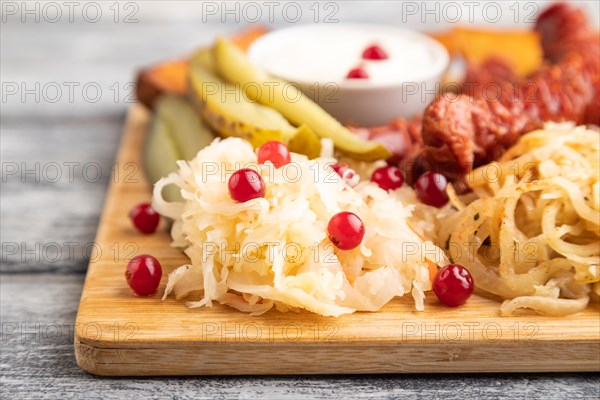 Set of snacks: sausages, toast, sauerkraut, marinated onion and cucumber, baked potato on a cutting board on a gray wooden background. Side view, close up, selective focus