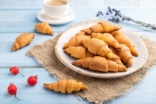 Homemade bagel roll with cup of coffee on a blue wooden background and linen textile. side view, close up