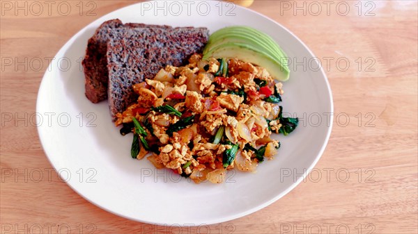 A plate of scrambled eggs with avocado and toast on a wooden table