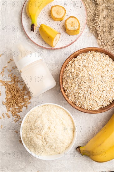 Powdered milk and oatmeal, banana baby food mix, infant formula, pacifier, bottle, spoon on gray concrete background. Top view, flat lay, artificial feeding concept