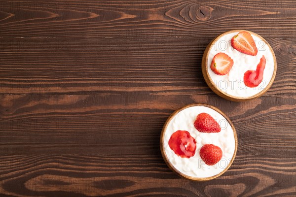 Grained cottage cheese with strawberry jam on brown wooden background. top view, flat lay, copy space