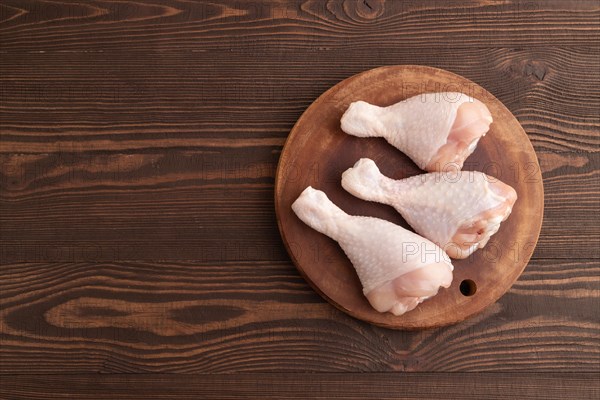 Raw chicken legs on a wooden cutting board on a brown wooden background. Top view, flat lay, copy space