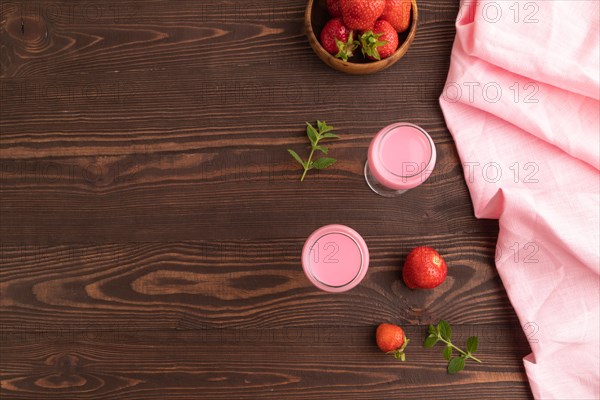 Sweet strawberry liqueur in glass on a brown wooden background and pink textile. top view, copy space, flat lay