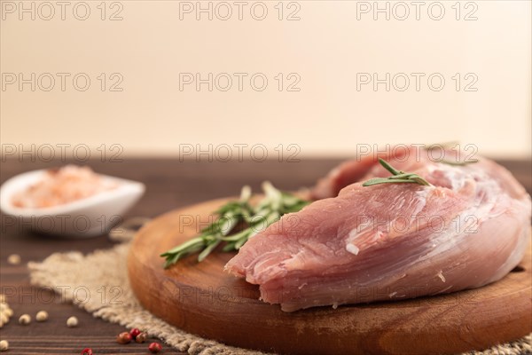 Raw pork with herbs and spices on a wooden cutting board on a brown wooden background. Side view, close up, selective focus