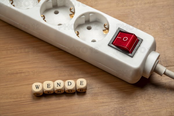 Concept image energy turnaround, switchable socket strip on wooden floor, letter cubes form the word turnaround, top view, studio image, Germany, Europe