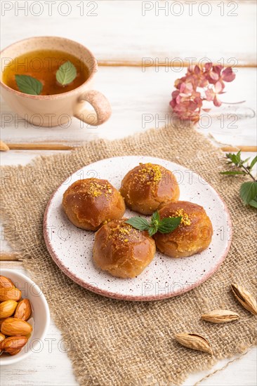 Homemade traditional turkish dessert sekerpare with almonds and honey, cup of green tea on white wooden background and linen textile. side view, close up