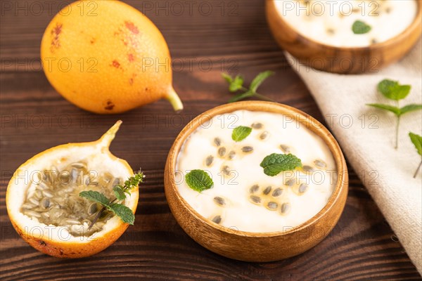 Yoghurt with granadilla and mint in wooden bowl on brown wooden background and linen textile. side view, close up, selective focus