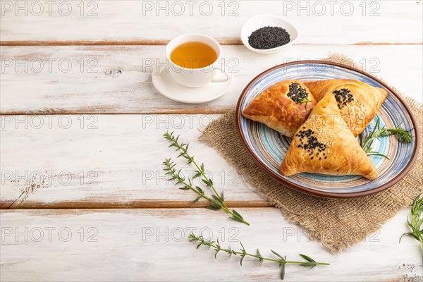 Homemade asian pastry samosa, cup of green tea on white wooden background and linen textile. side view, copy space