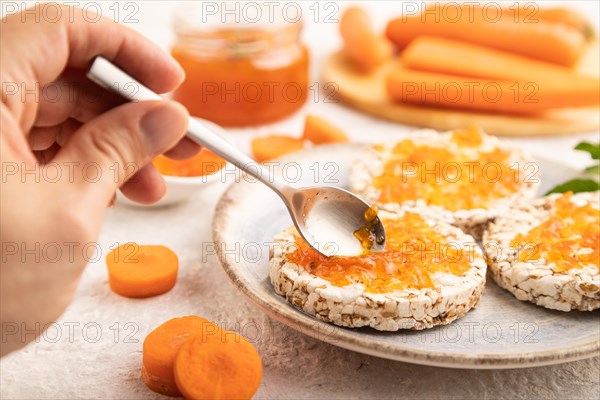 Carrot jam with puffed rice cakes on gray concrete background with hand. Side view, close up, selective focus