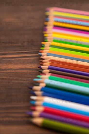 Set of watercolor pencils on brown wooden background. Side view, close up, selective focus