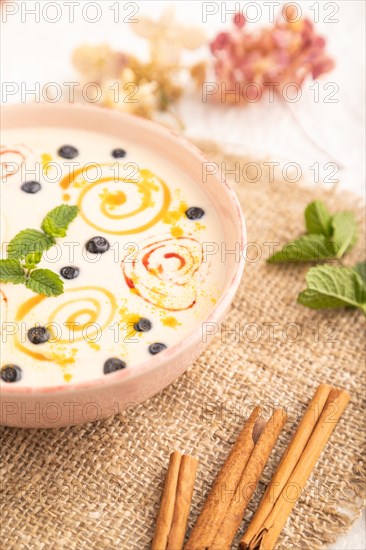 Yoghurt with bilberry and caramel in ceramic bowl on gray concrete background and linen textile. side view, close up, selective focus