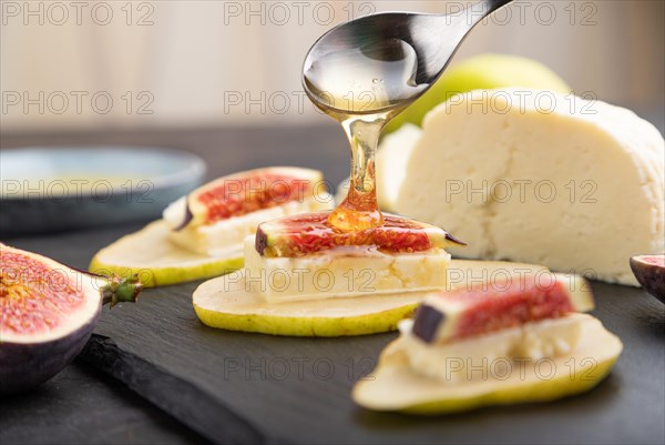 Summer appetizer with pear, cottage cheese, figs and honey on slate board on a black concrete background. Side view, close up, selective focus