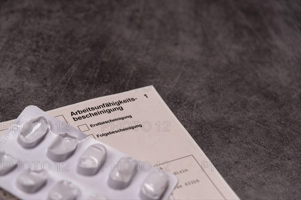 Blister pack with pills next to a certificate of incapacity for work on a grey stone slab, studio photograph, Germany, Europe