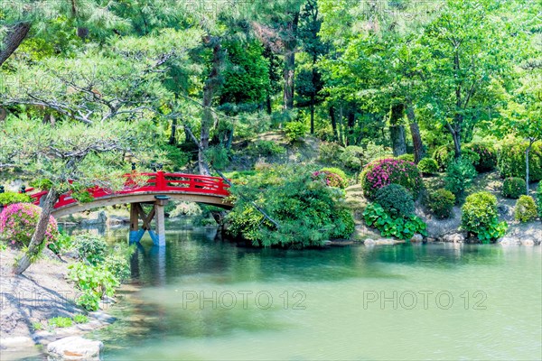 Red wooden footbridge over man made pond in Japanese garden in Hiroshima, Japan, Asia