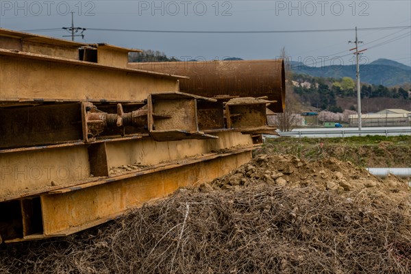 Stack of rusted metal beams and pipe in countryside under dull overcast sky