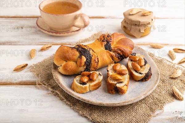 Homemade sweet bun with honey almonds and cup of green tea on a white wooden background and linen textile. side view, close up