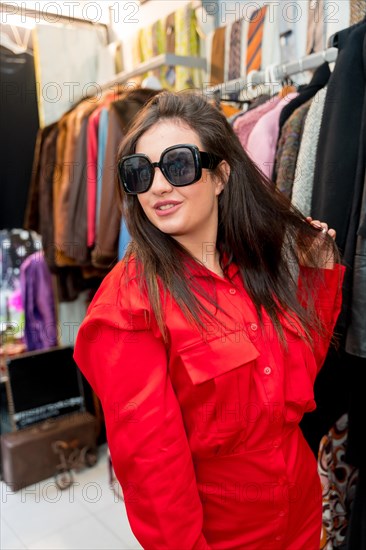 Vertical photo of a woman posing while trying on second hand clothes in a vintage store