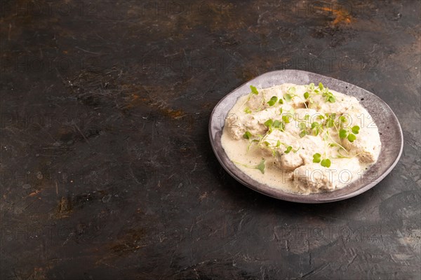 Stewed chicken fillets with coconut milk sauce and rucola microgreen on black concrete background. side view, copy space