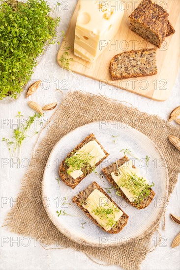 Grain bread sandwiches with cheese and watercress microgreen on gray concrete background and linen textile. side view, close up