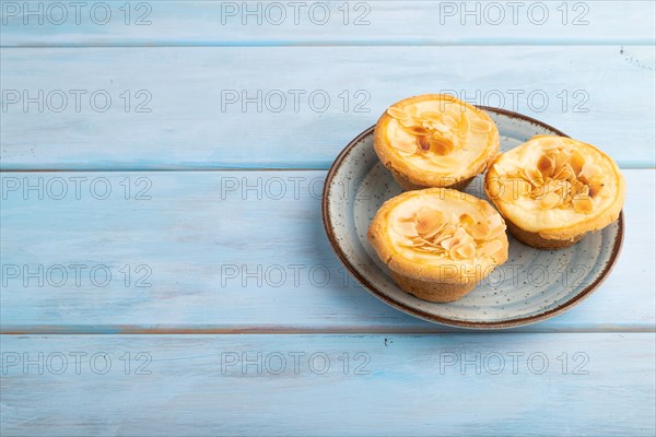 Traditional portuguese cakes pasteis de nata, custard small pies with almonds on blue wooden background. Side view, copy space
