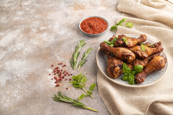 Smoked chicken legs with herbs and spices on a ceramic plate with linen textile on a brown concrete background. Side view, copy space