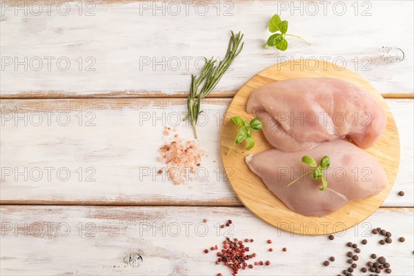 Raw chicken breast with herbs and spices on a wooden cutting board on a white wooden background. Top view, flat lay, copy space