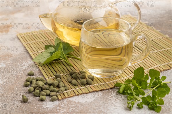 Green oolong tea with herbs in glass on brown concrete background. Healthy drink concept. Side view, close up
