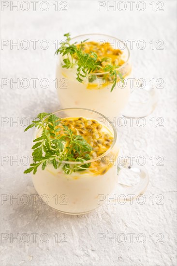 Yogurt with passionfruit and marigold microgreen in glass on gray concrete background. Side view, close up