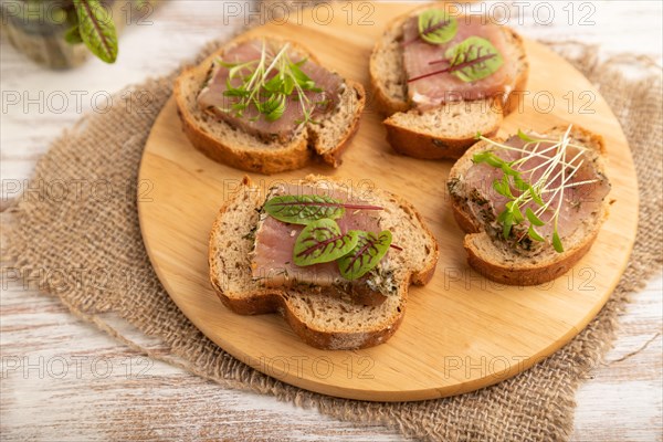 Bread sandwiches with jerky salted meat, sorrel and cilantro microgreen on white wooden background and linen textile. side view, close up, selective focus